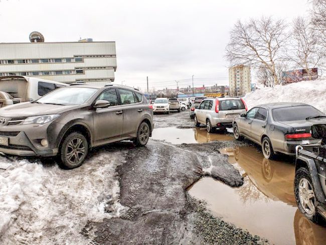 На стоянке камчатского Центробанке уровень доходов видно по тачкам. И рядом разбитая в хлам дорога, в слякоть грязюка, кругом мусор.
